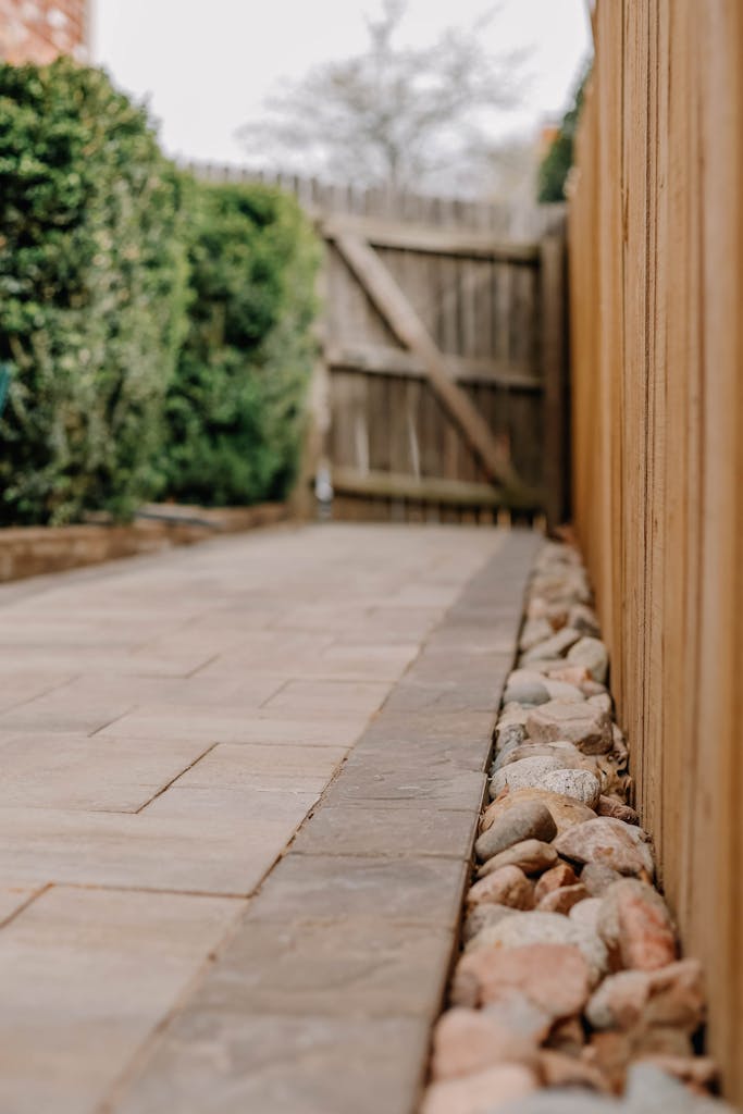 A serene view of a backyard paved stone path flanked by wooden fence and green bushes.